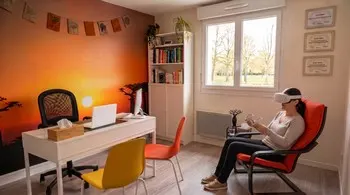 Vue de l'intérieur du cabinet de Céline Schaar à Nozay : bureau, mur décoré d'un coucher de soleil sur l'Afrique avec baobabs et patiente en fauteuil utilisant un casque de réalité virtuelle pour une thérapie.